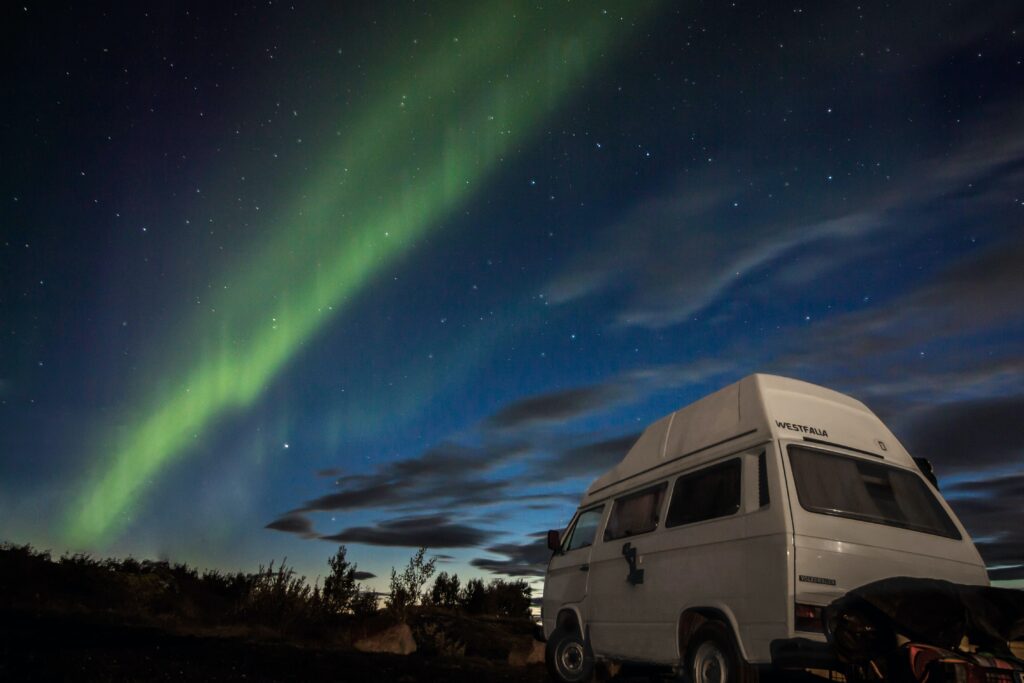 A campervan parked in nature with northern lights in the background